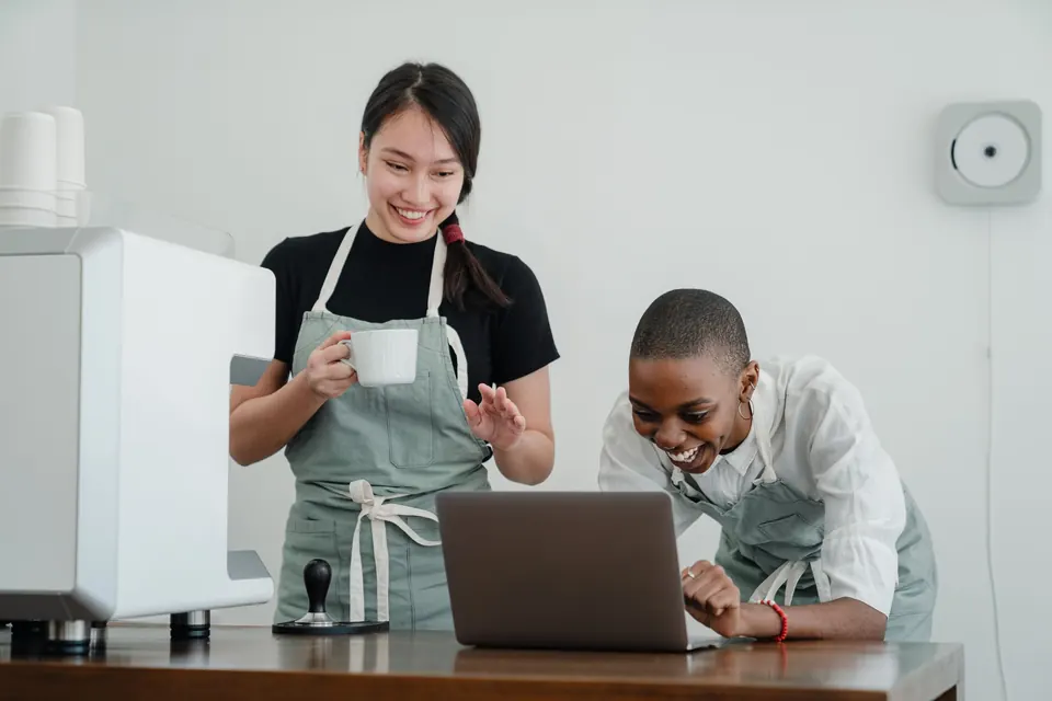 Deux commerçantes regardent leurs ventes sur un ordinateur portable, en riant