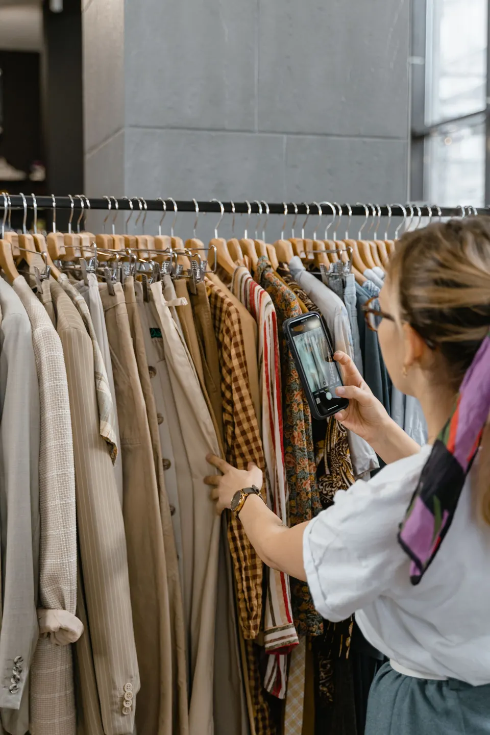 Une vendeuse photographie les vêtements de son portant avec son téléphone
