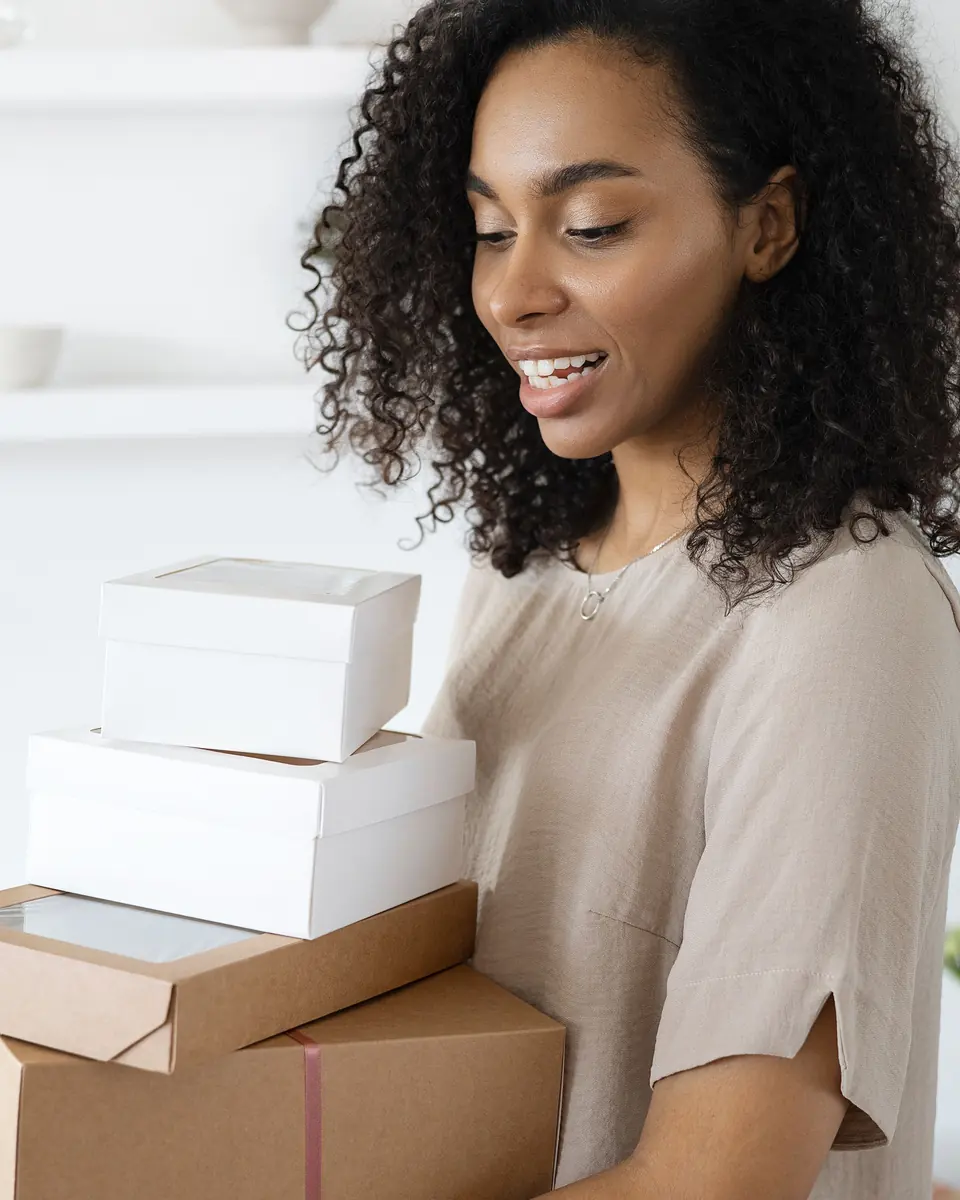 Une vendeuse aux cheveux afro sourit en portant les colis de sa boutique en ligne